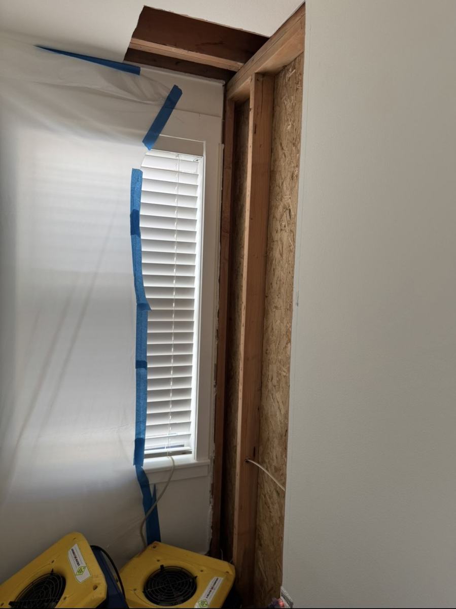 Before — wall opened to exposed framing after water damage, drying fans running